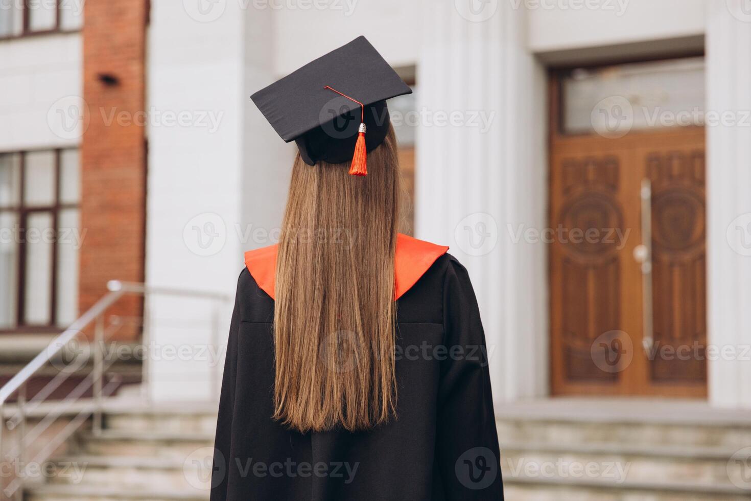 Rear View of Female Graduate in Cap and Gown Standing Outside University Building photo