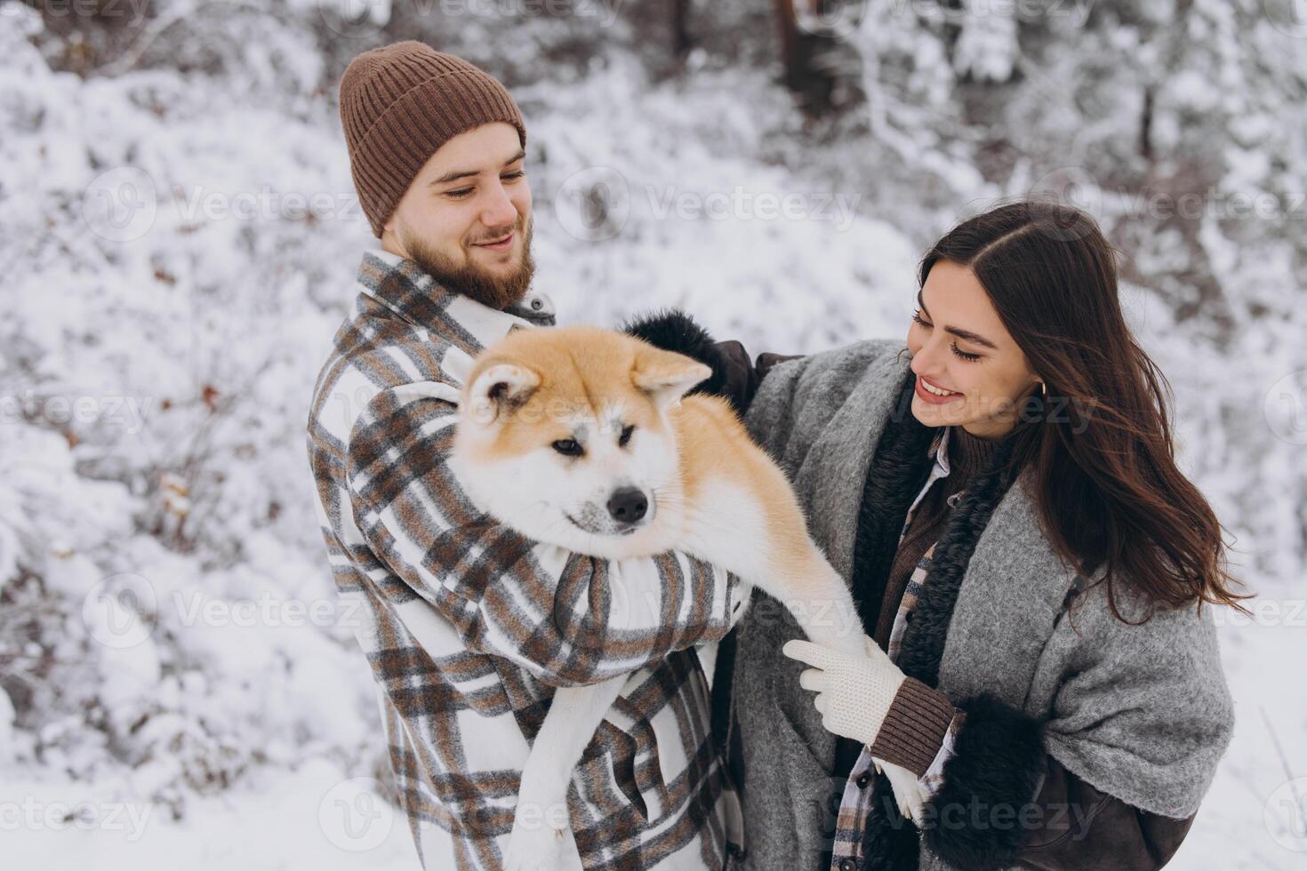 Happy young couple with akita dog in forest on winter day photo