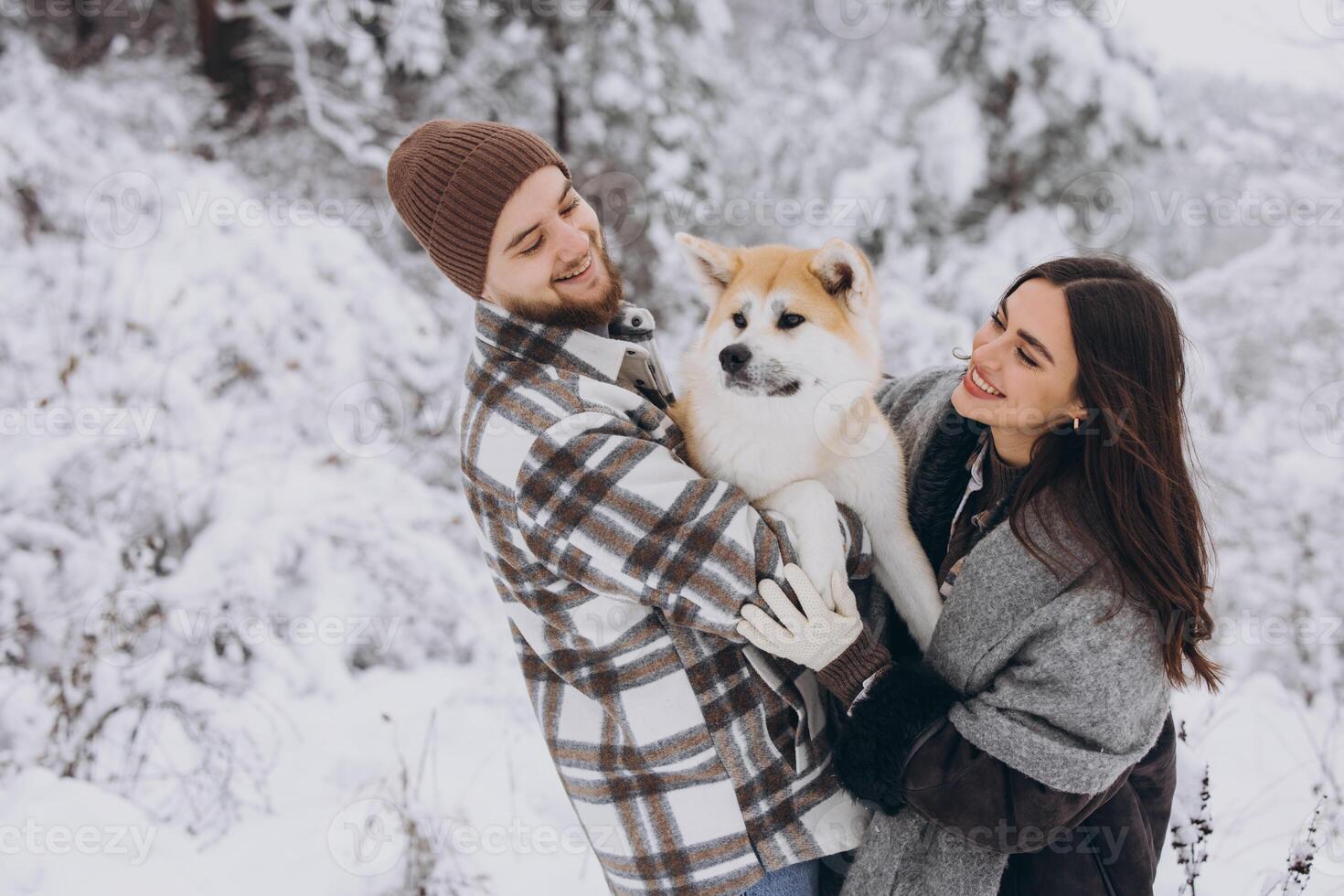 Happy young couple with akita dog in forest on winter and snowly day photo