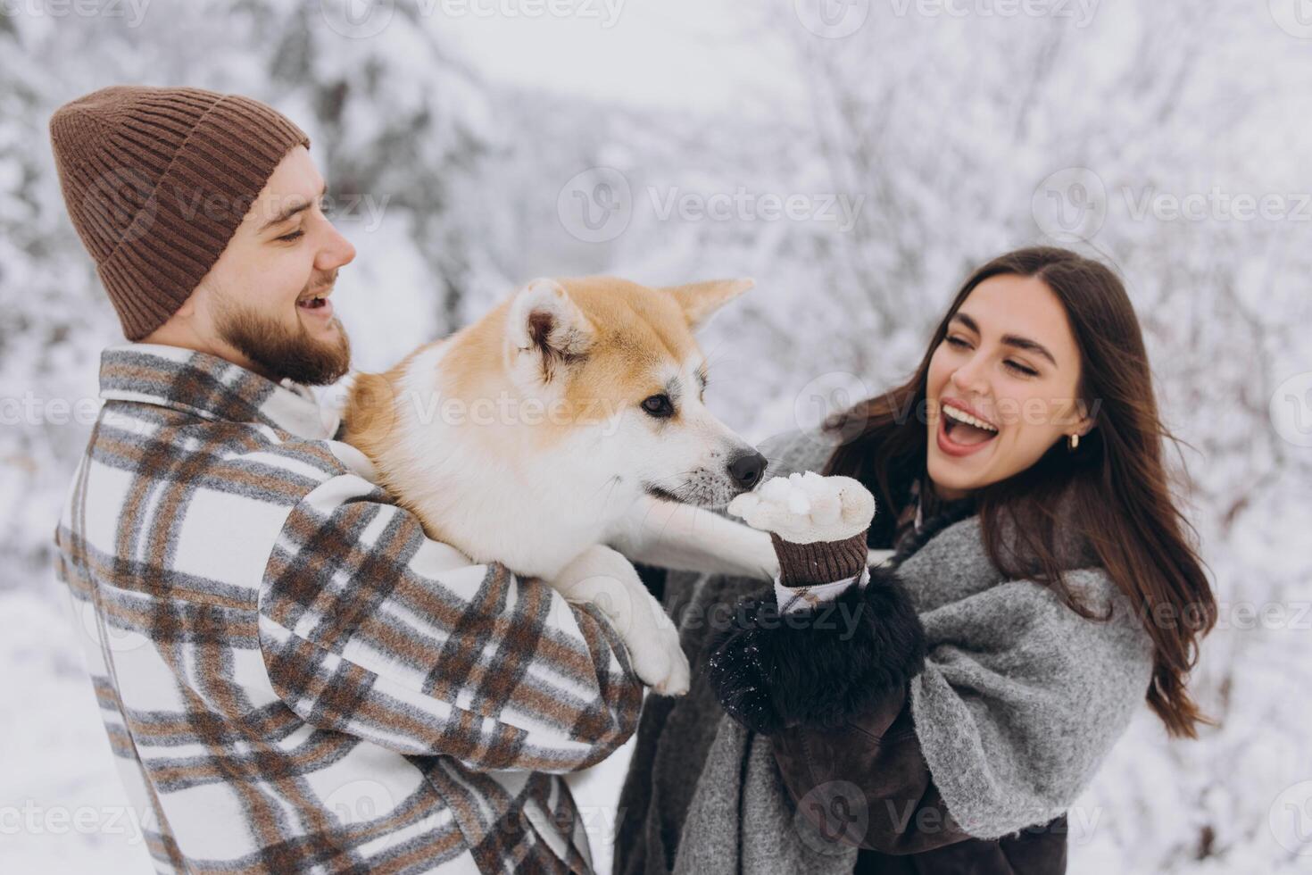 Happy young couple with akita dog in forest on winter and snowly day photo