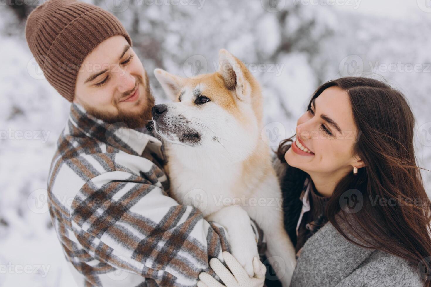 Happy young couple with akita dog in forest on winter and snowly day photo
