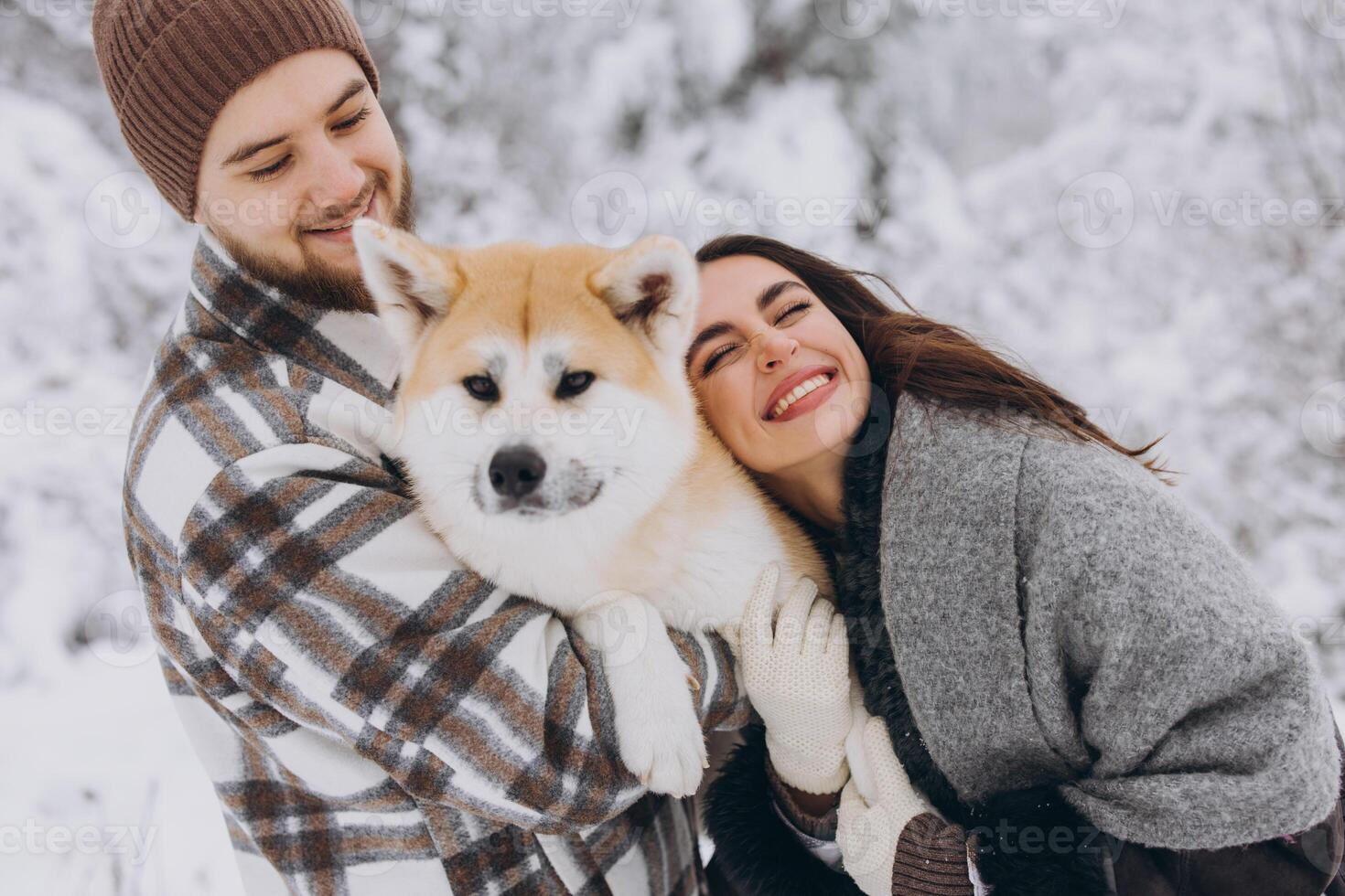 Happy young couple with akita dog in forest on winter and snowly day photo