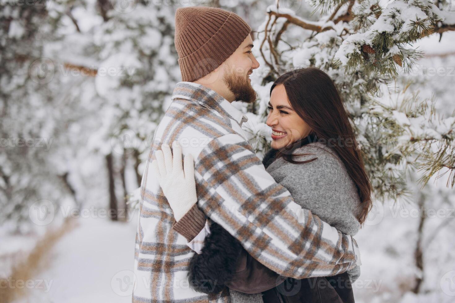 A young happy and loving couple is standing under a pine tree from which snow falls in the mountains in winter. photo