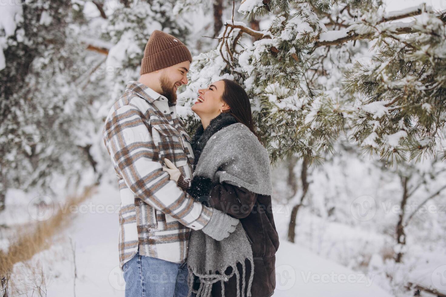 A young happy and loving couple is standing under a pine tree from which snow falls in the mountains in winter. photo