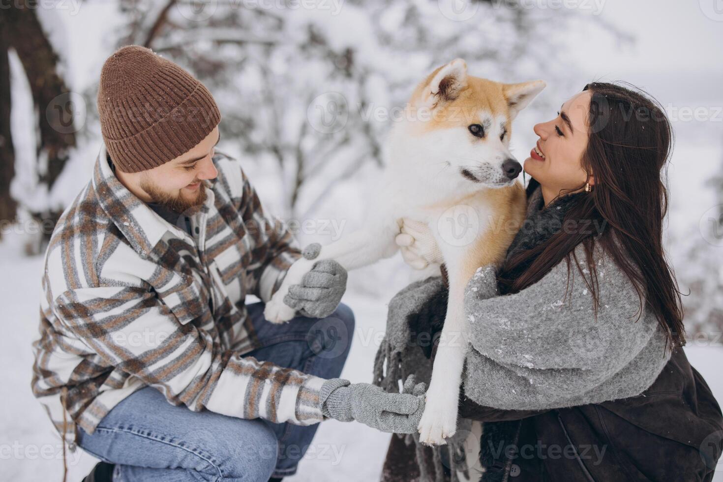 Happy young couple walking with akita dog in forest on winter and snowly day photo