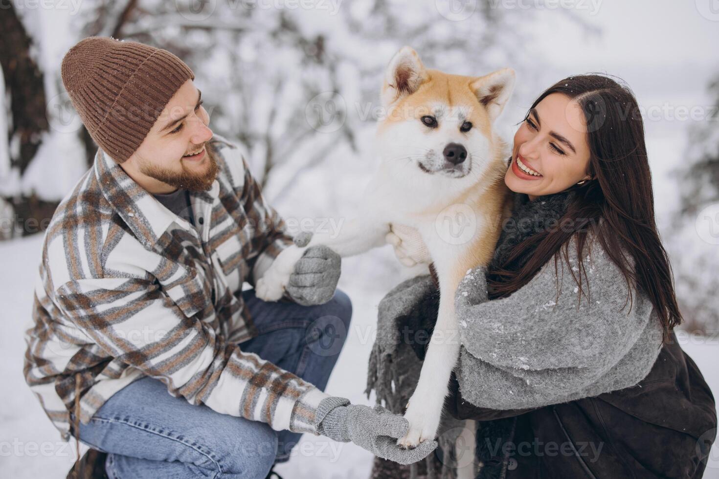 Happy young couple walking with akita dog in forest on winter and snowly day photo