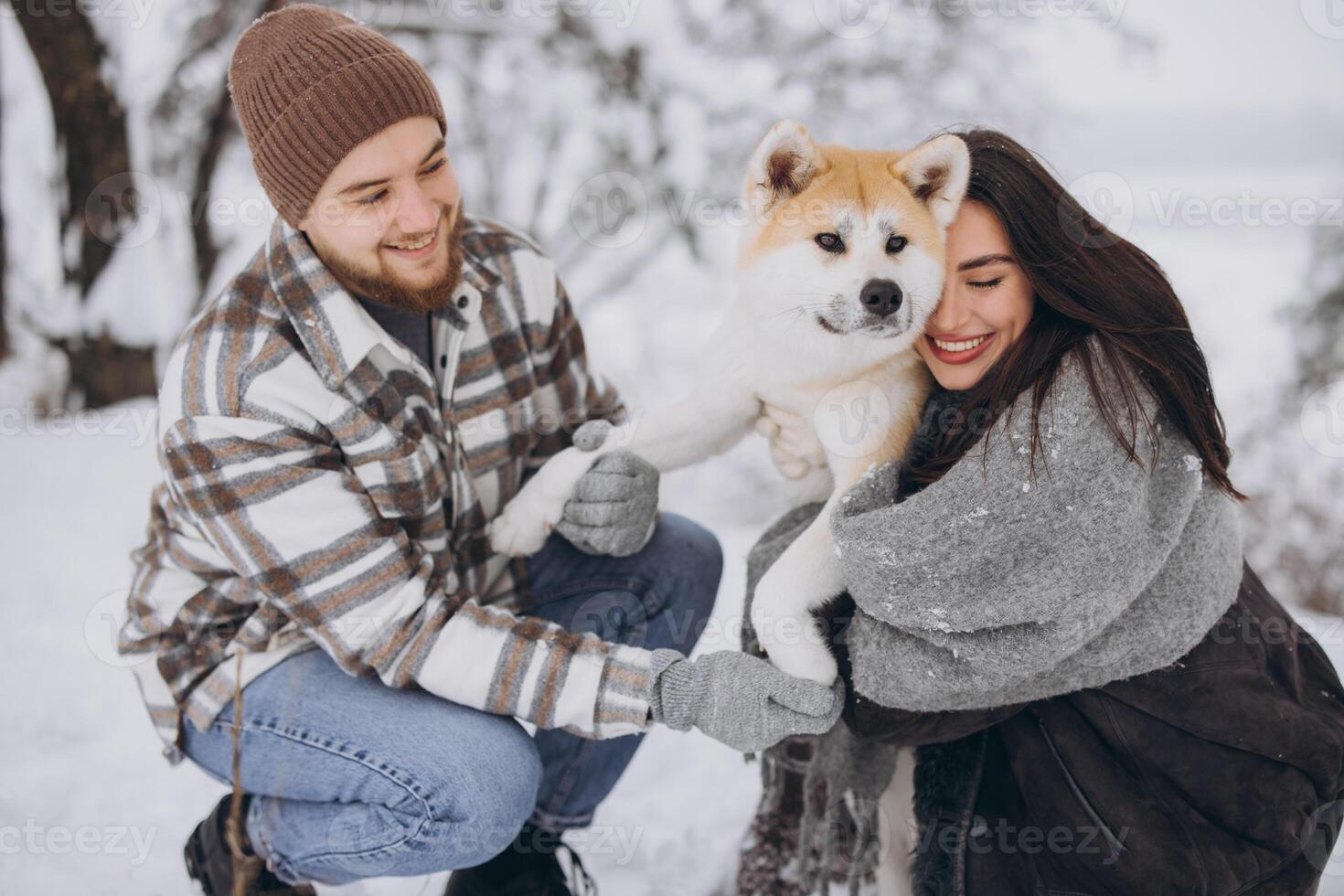 Happy young couple walking with akita dog in forest on winter and snowly day photo