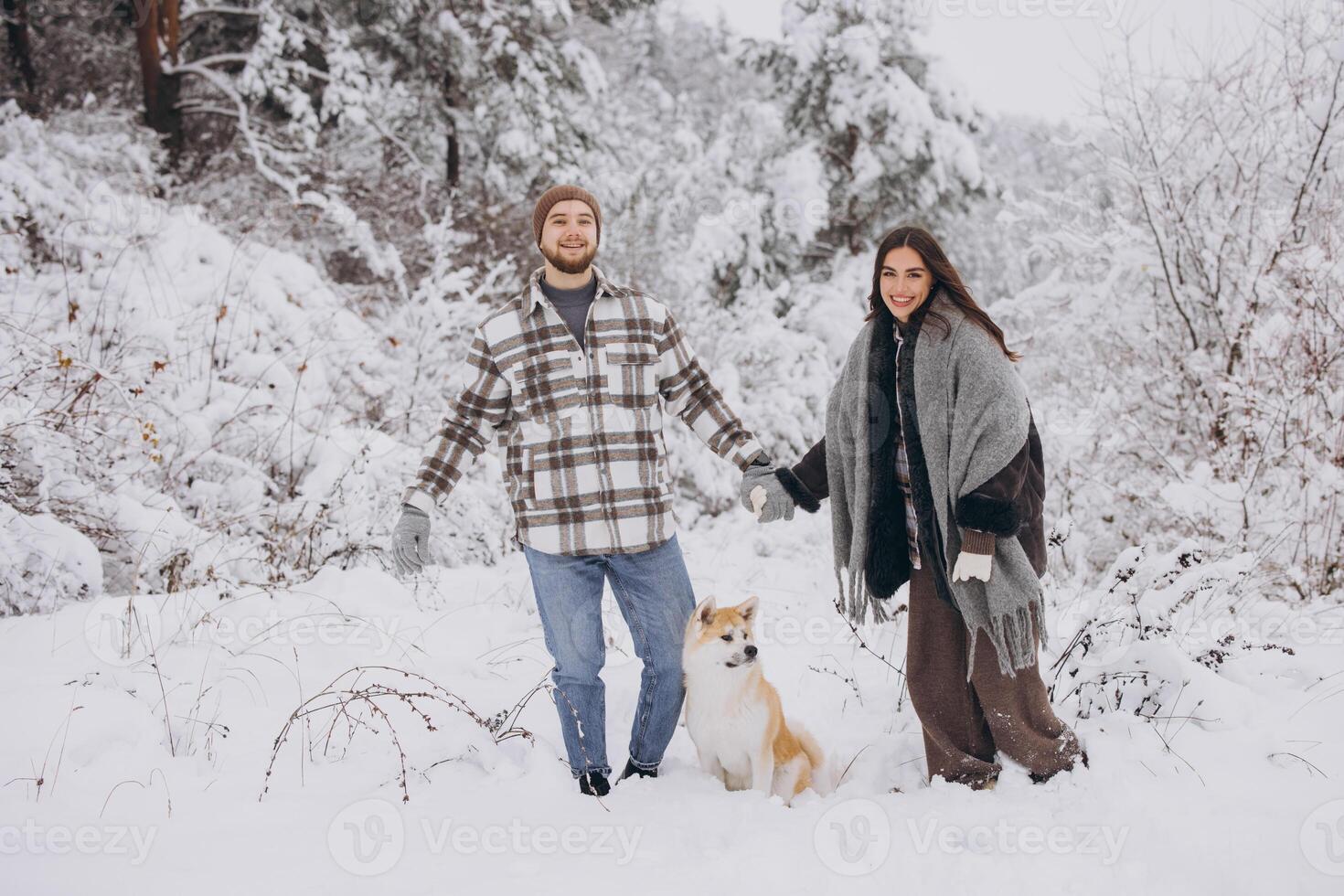Happy young couple with akita dog in forest on winter and snowly day photo