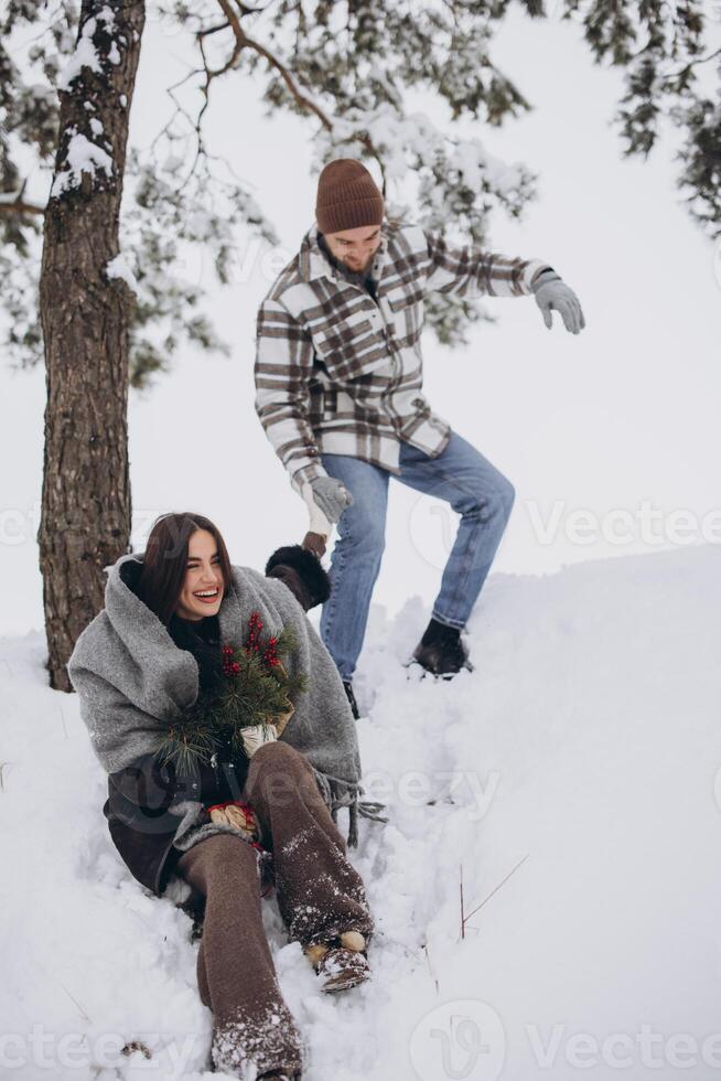 Cute young couple in love with pine bouquet spending time on Valentine's day in snowy winter forest in mountains photo