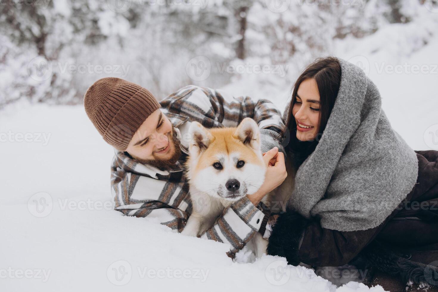 Happy young couple with akita dog in forest on winter day photo