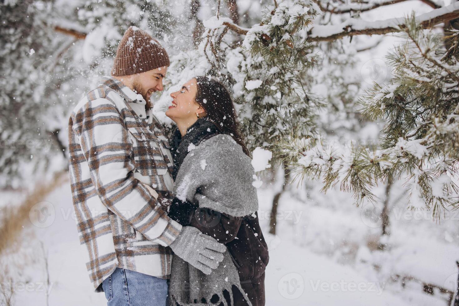 A young happy and loving couple is standing under a pine tree from which snow falls in the mountains in winter. photo