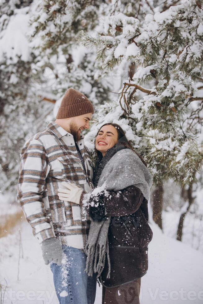 A young happy and loving couple is standing under a pine tree from which snow falls in the mountains in winter. photo