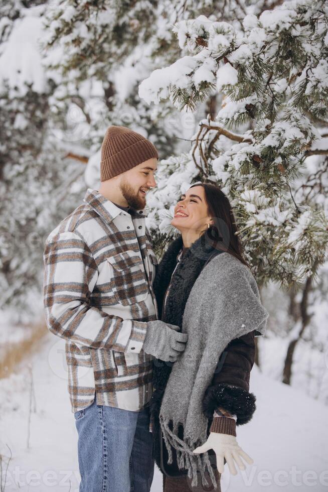 A young happy and loving couple is standing under a pine tree from which snow falls in the mountains in winter. photo