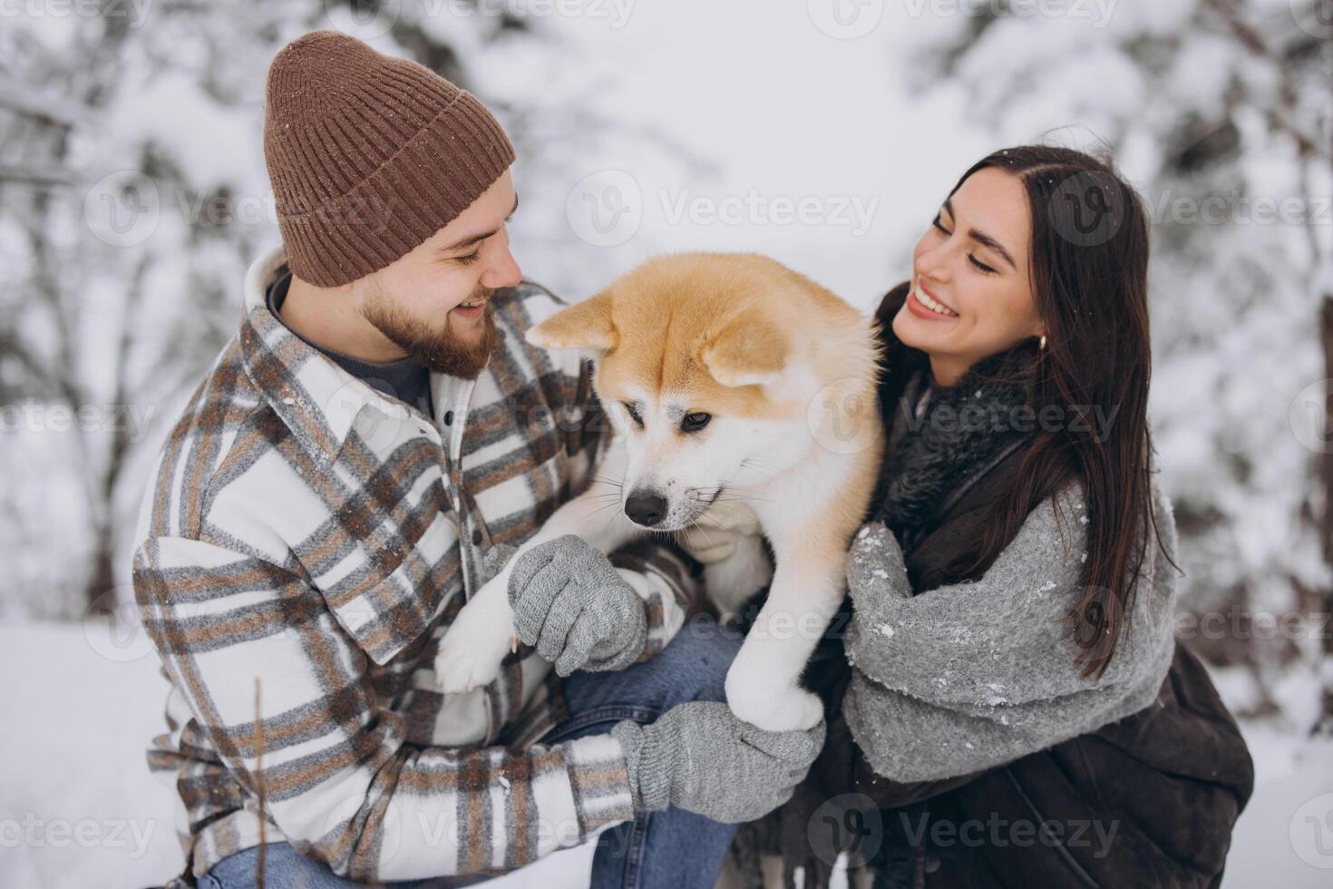 Happy young couple walking with akita dog in forest on winter and snowly day photo