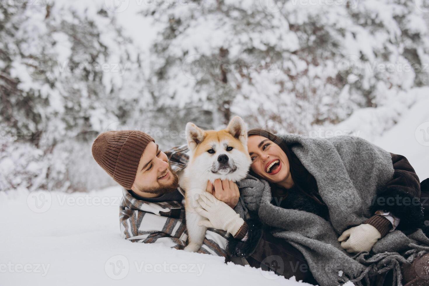 Happy young couple with akita dog in forest on winter day photo