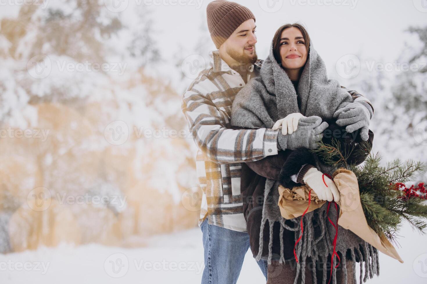 Cute young couple in love with pine bouquet spending time on Valentine's day in snowy winter forest in mountains photo