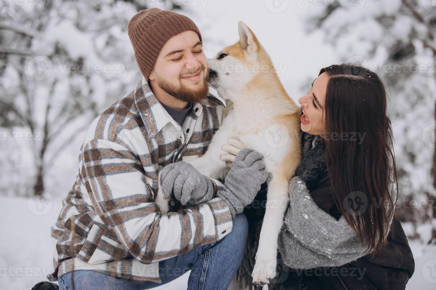 Happy young couple walking with akita dog in forest on winter and snowly day photo