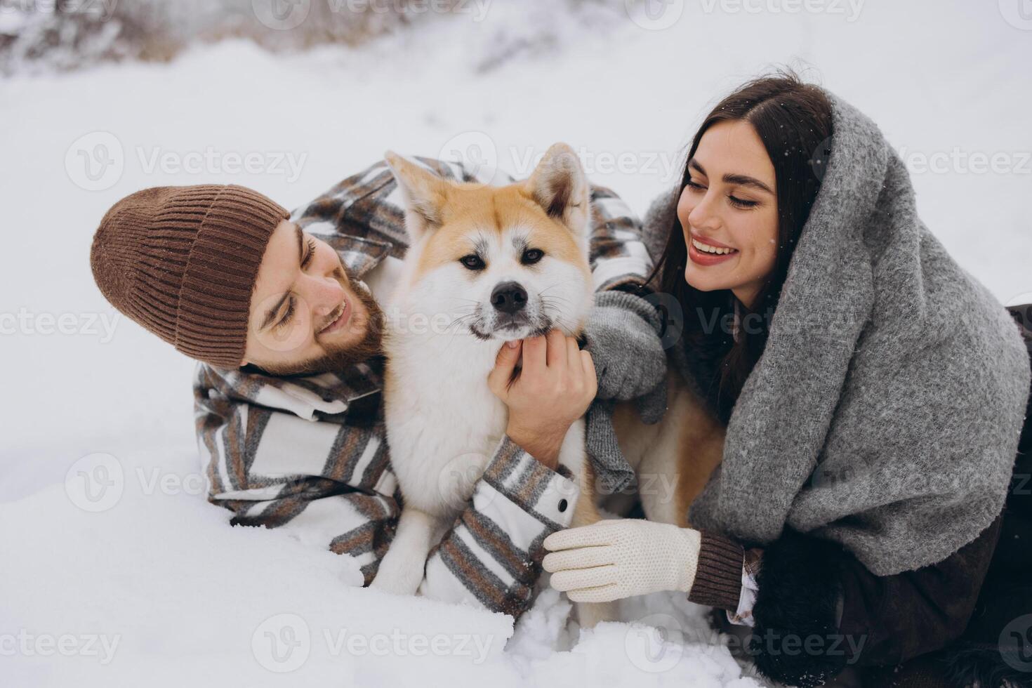 Happy young couple with akita dog in forest on winter day photo