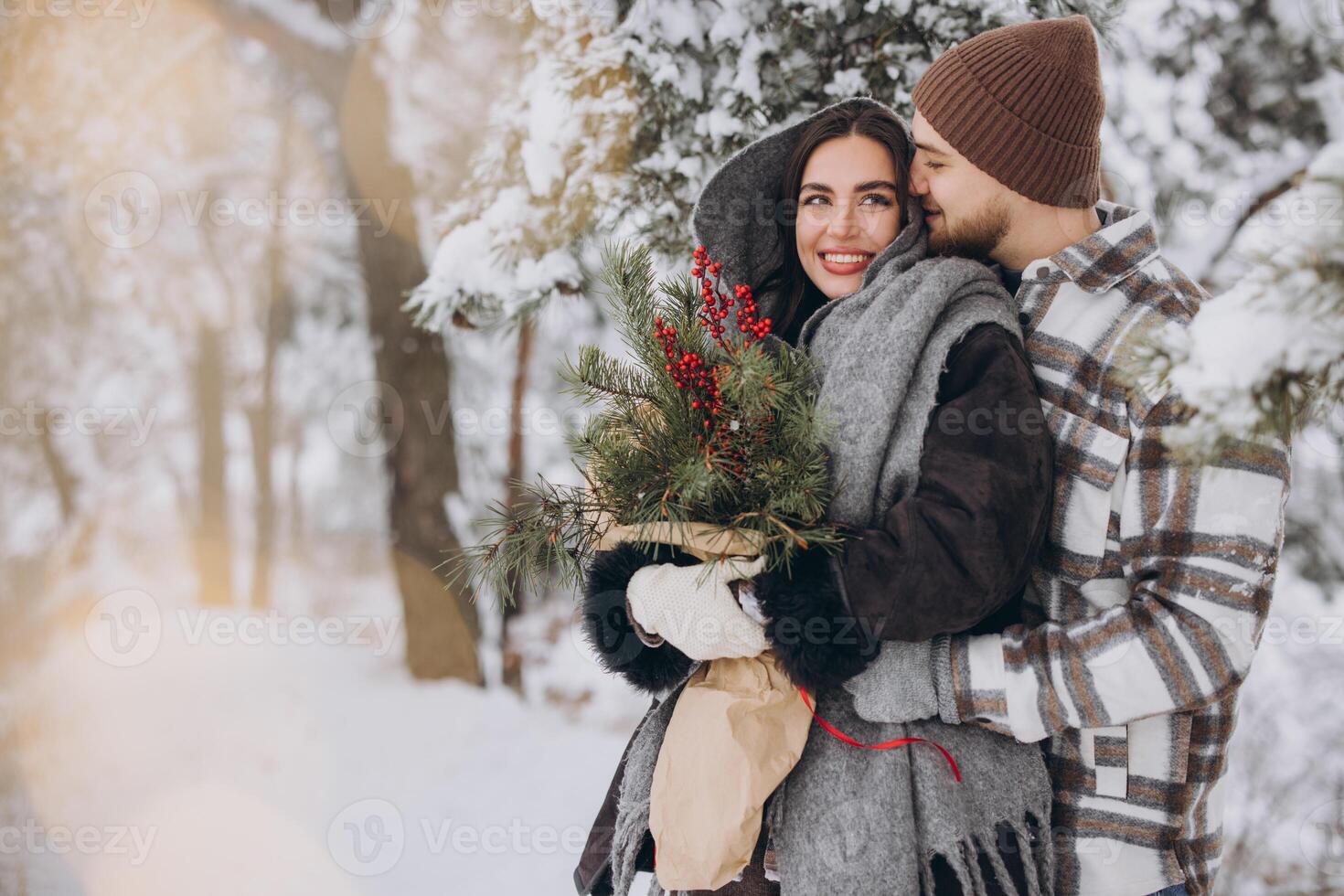 Cute young couple in love with pine bouquet spending time on Valentine's day in snowy winter forest in mountains photo
