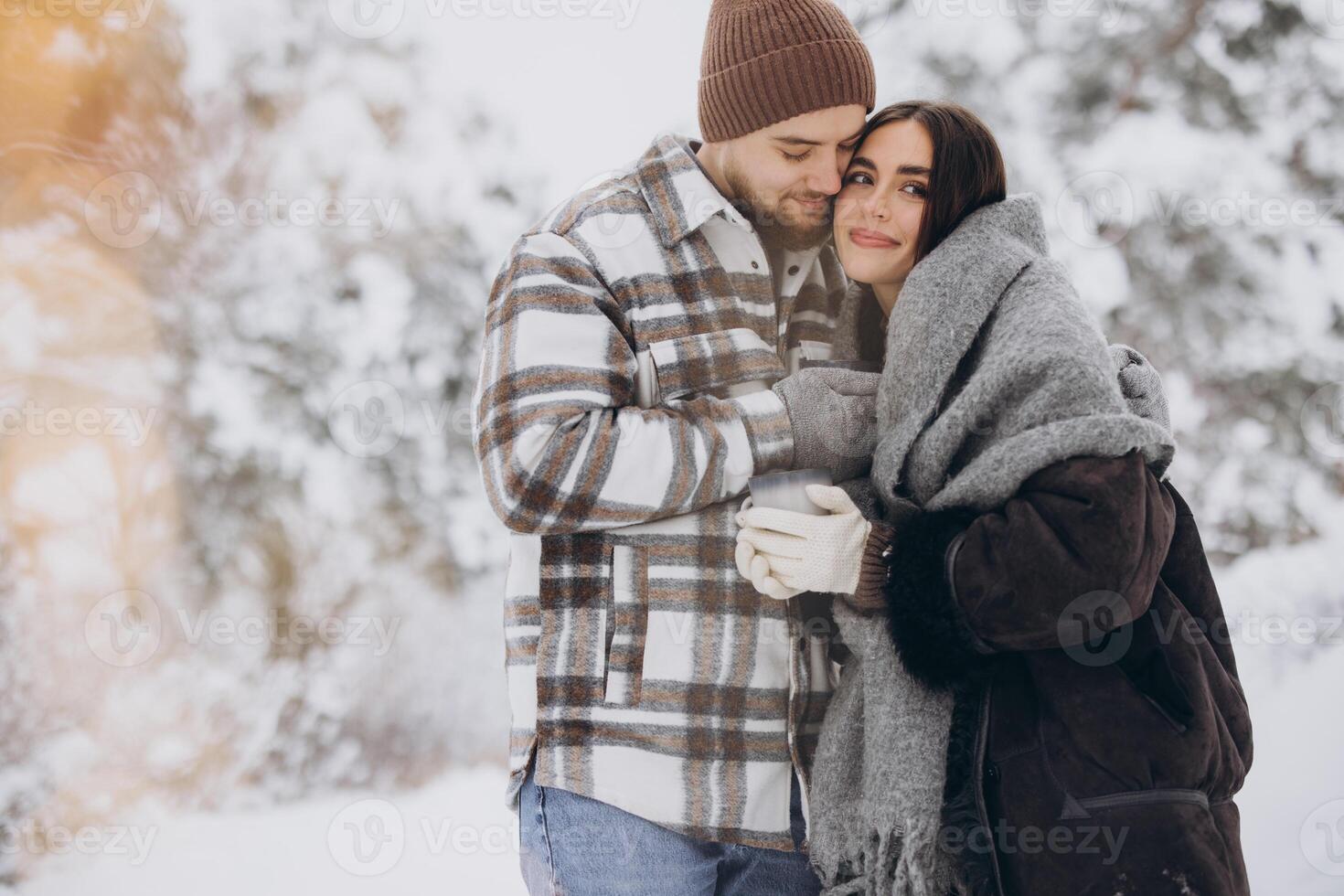 Happy beautiful couple resting and drinking hot tea in the forest in winter in the mountains photo