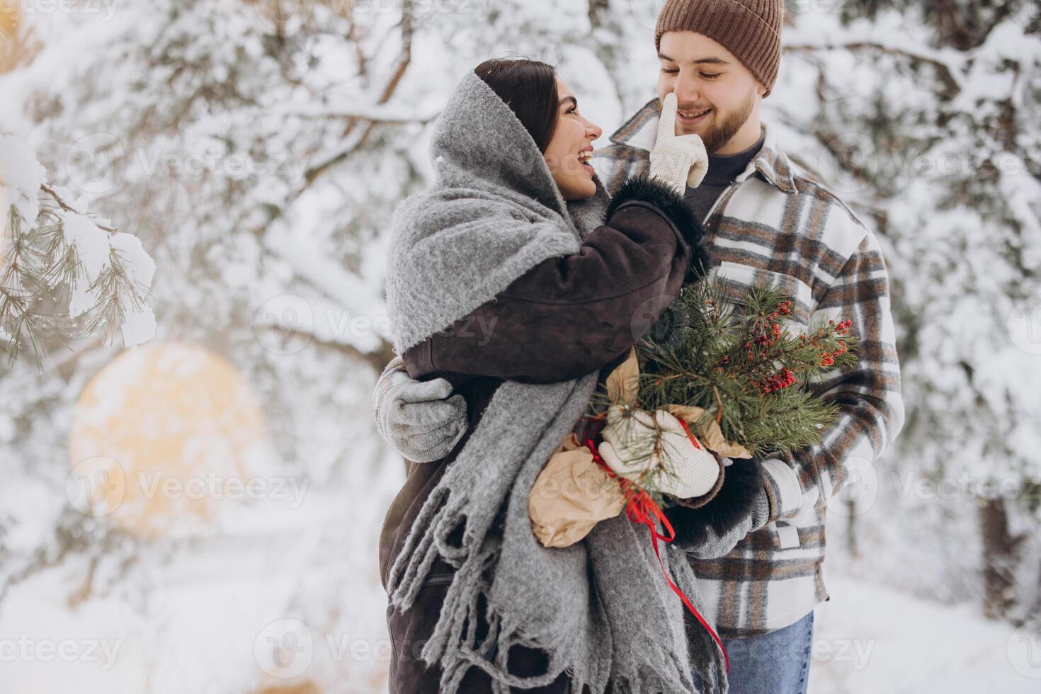 Cute young couple in love with pine bouquet spending time on Valentine's day in snowy winter forest in mountains photo