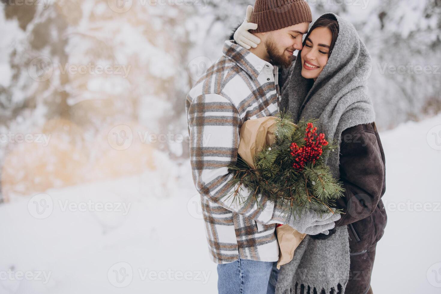 Cute young couple in love with pine bouquet spending time on Valentine's day in snowy winter forest in mountains photo