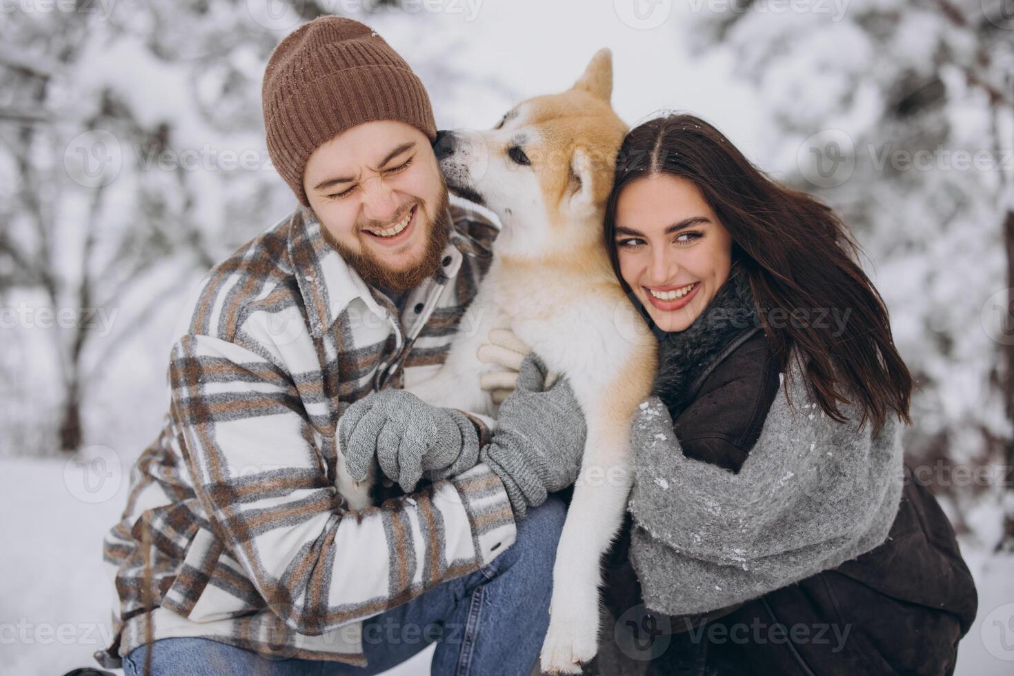 Happy young couple walking with akita dog in forest on winter and snowly day photo
