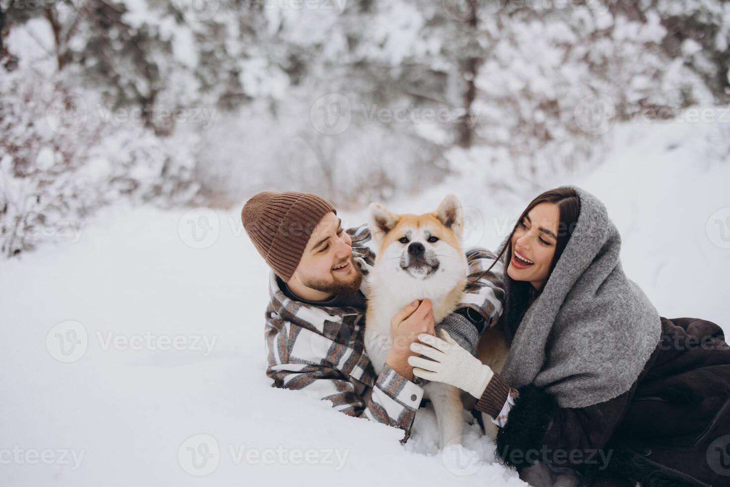 Happy young couple with akita dog in forest on winter day photo