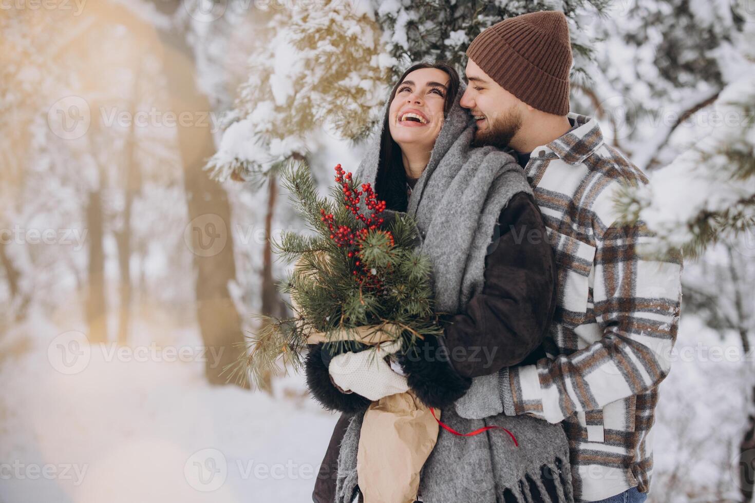 Cute young couple in love with pine bouquet spending time on Valentine's day in snowy winter forest in mountains photo