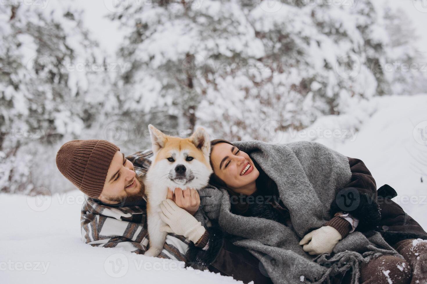 Happy young couple with akita dog in forest on winter day photo
