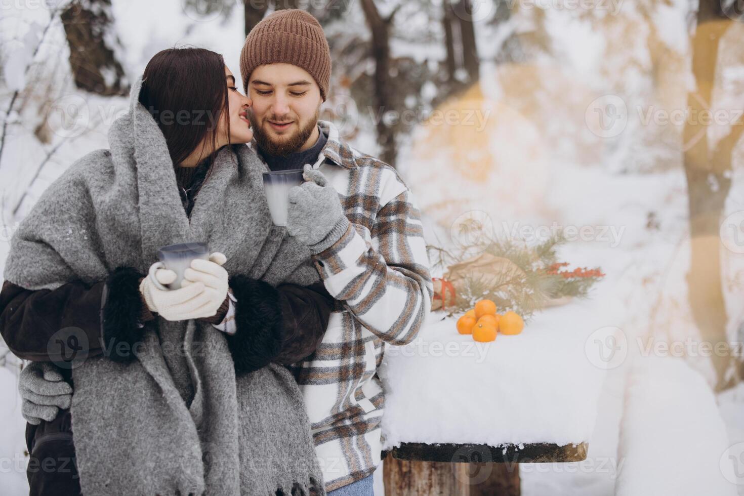 Happy beautiful couple resting and drinking hot tea in the forest in winter in the mountains photo