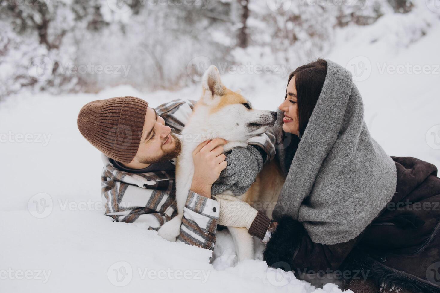 Happy young couple with akita dog in forest on winter day photo
