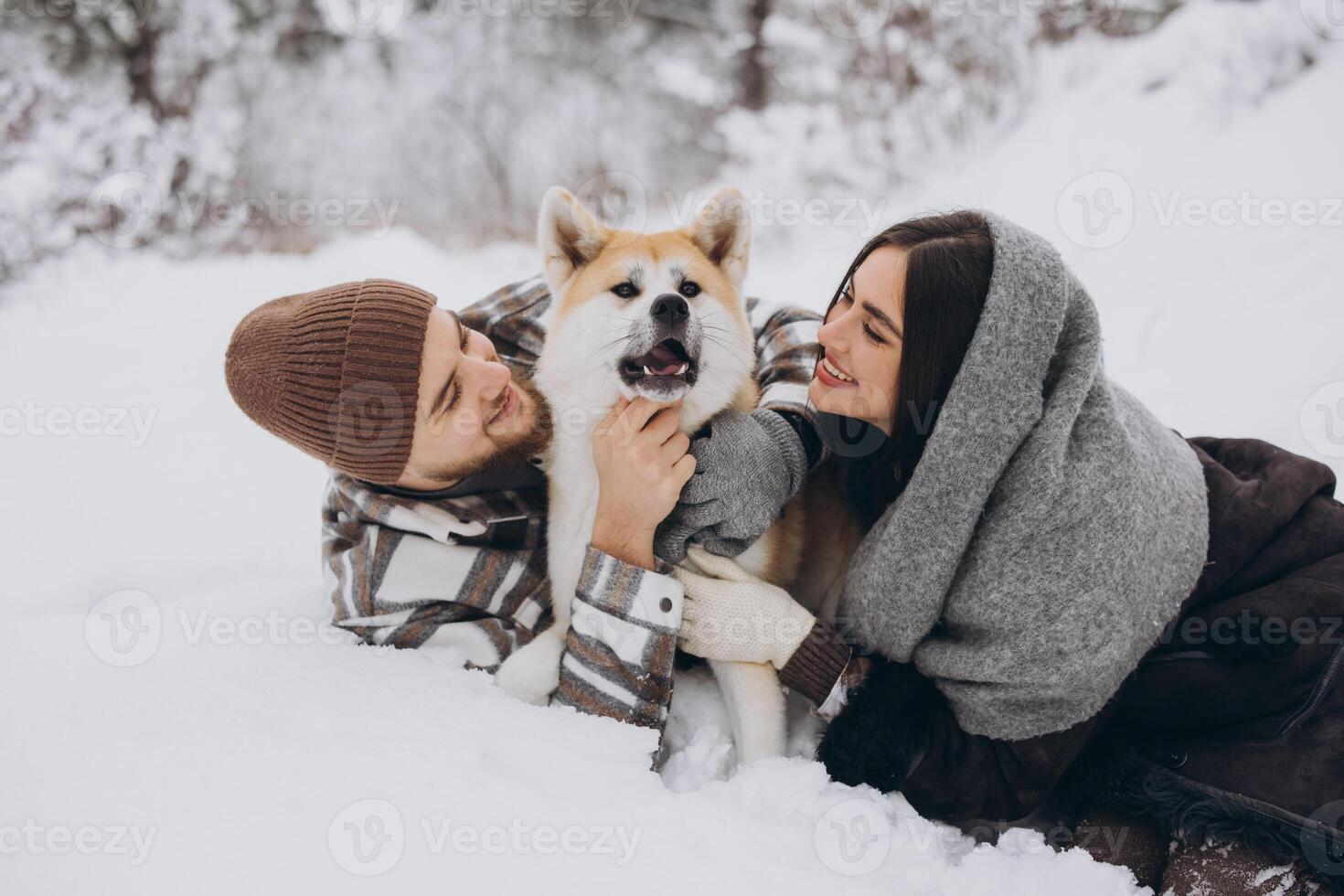 Happy young couple with akita dog in forest on winter day photo
