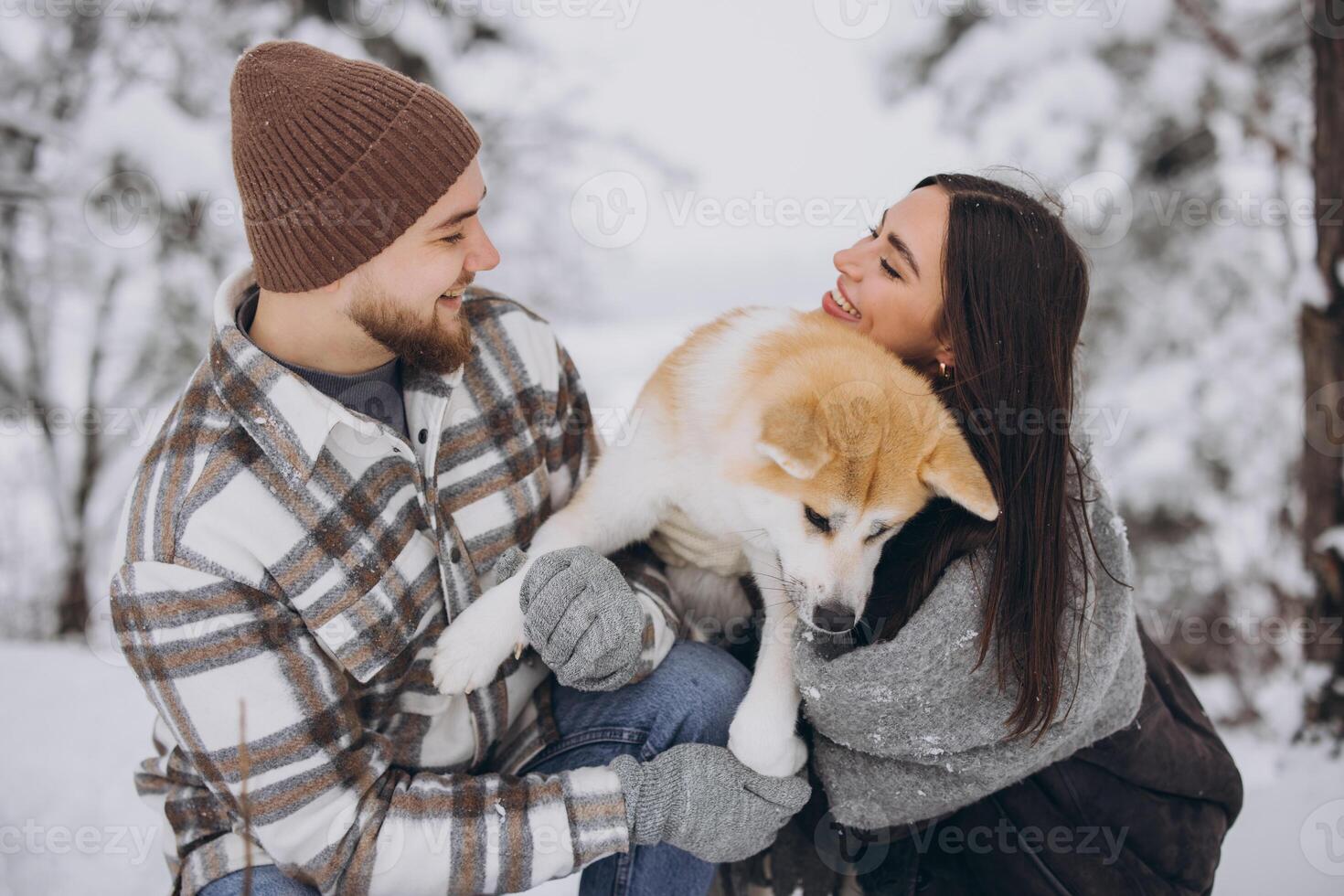 Happy young couple walking with akita dog in forest on winter and snowly day photo