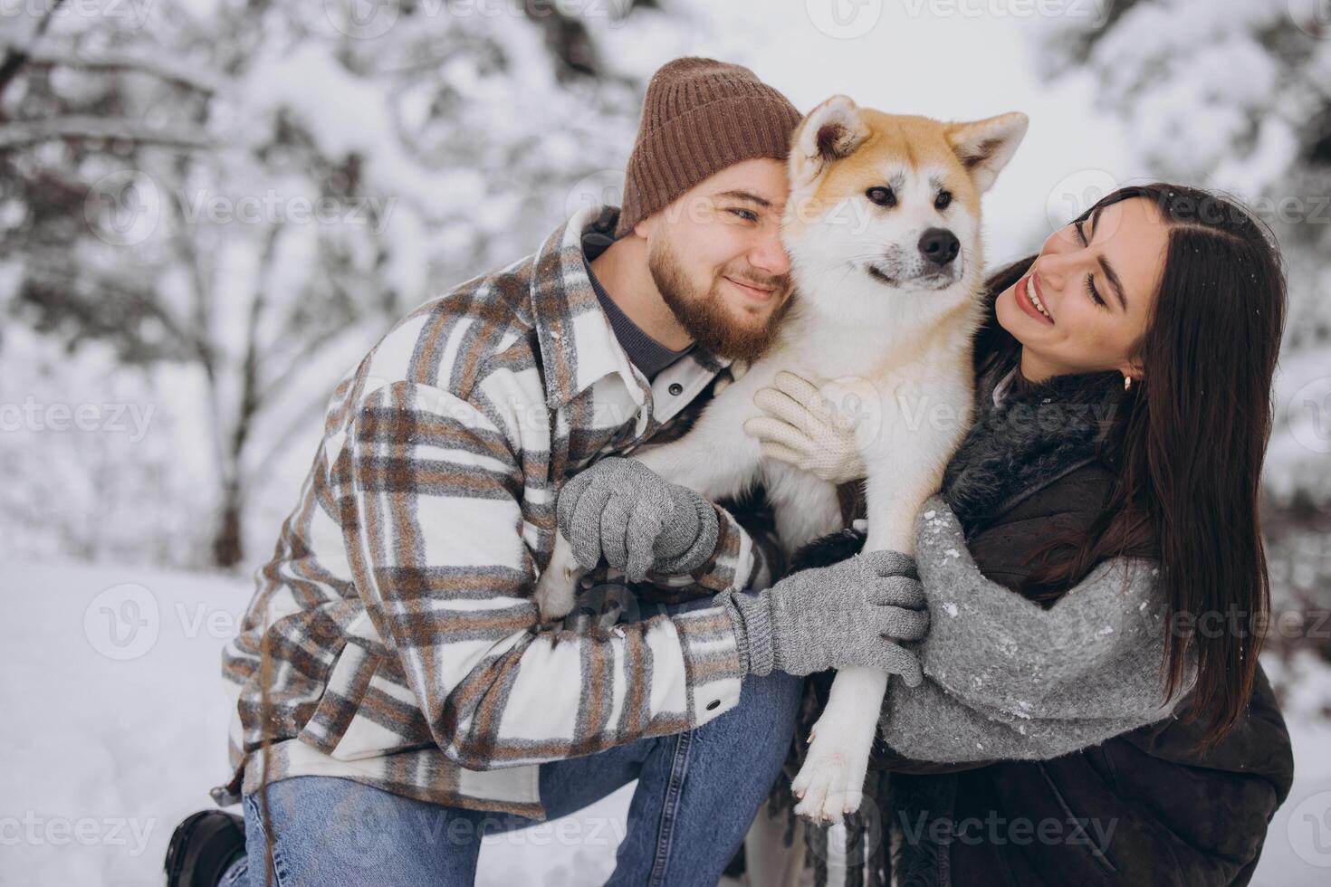 Happy young couple walking with akita dog in forest on winter and snowly day photo