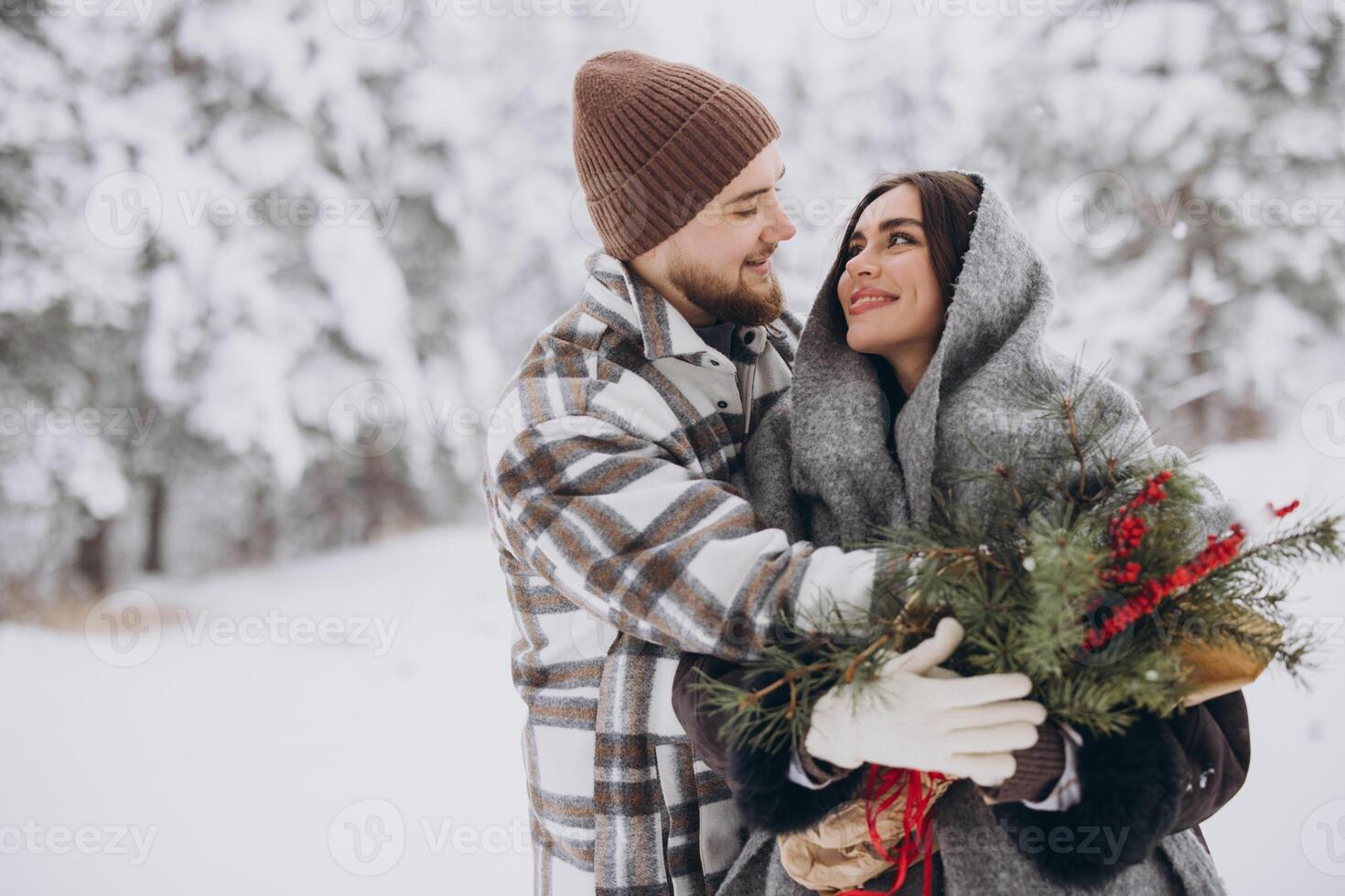 Cute young couple in love with pine bouquet spending time on Valentine's day in snowy winter forest in mountains photo