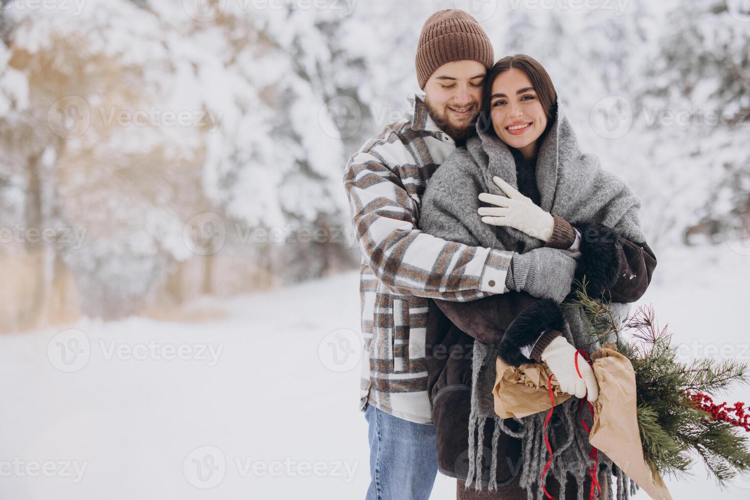 Cute young couple in love with pine bouquet spending time on Valentine's day in snowy winter forest in mountains photo