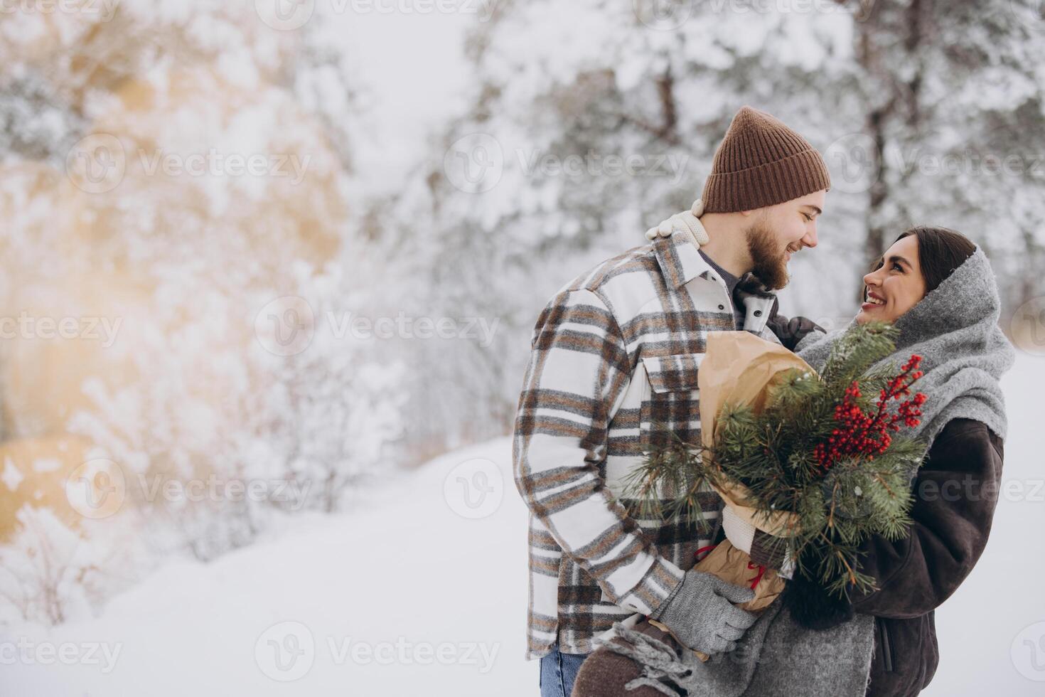 Cute young couple in love with pine bouquet spending time on Valentine's day in snowy winter forest in mountains photo
