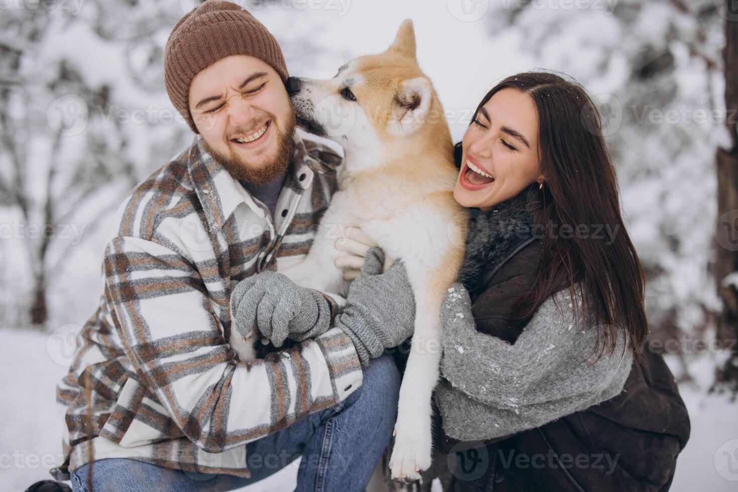 Happy young couple walking with akita dog in forest on winter and snowly day photo