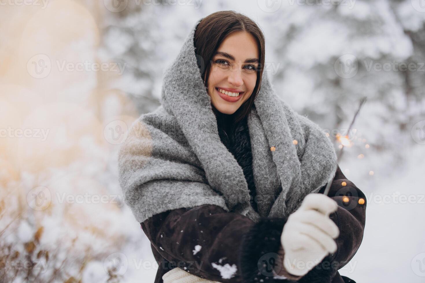 Portrait of happy pretty woman in knitted scarf and mittens holding sparkler and posing in snowy forest photo
