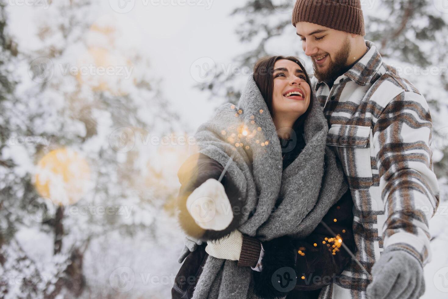 Happy romantic couple in love holding sparklers in snowy winter forest photo