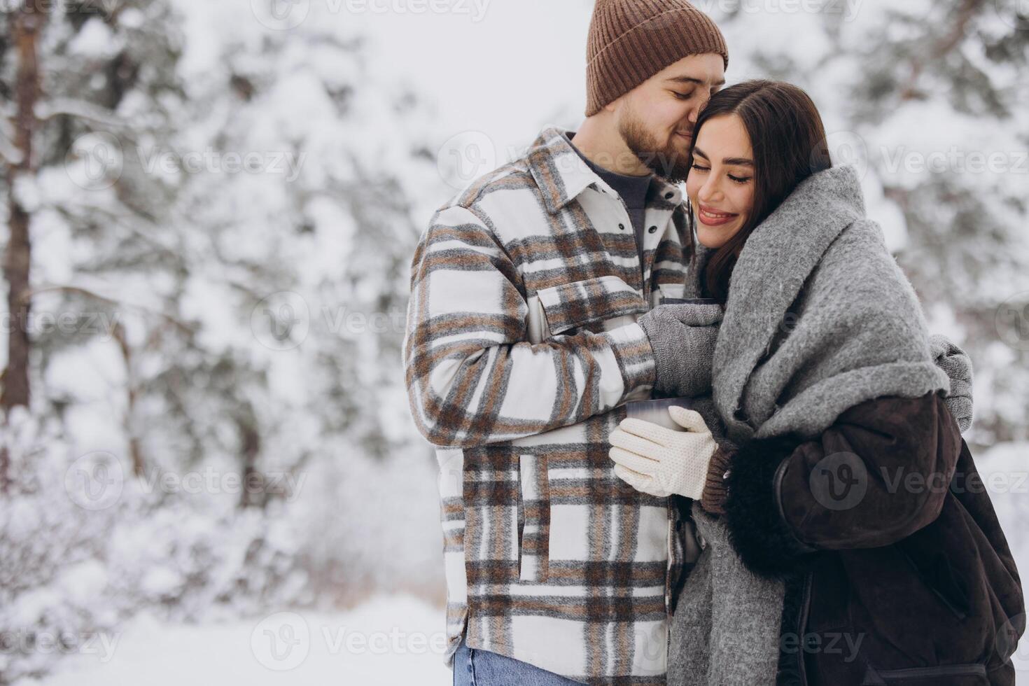Happy beautiful couple resting and drinking hot tea in the forest in winter in the mountains photo