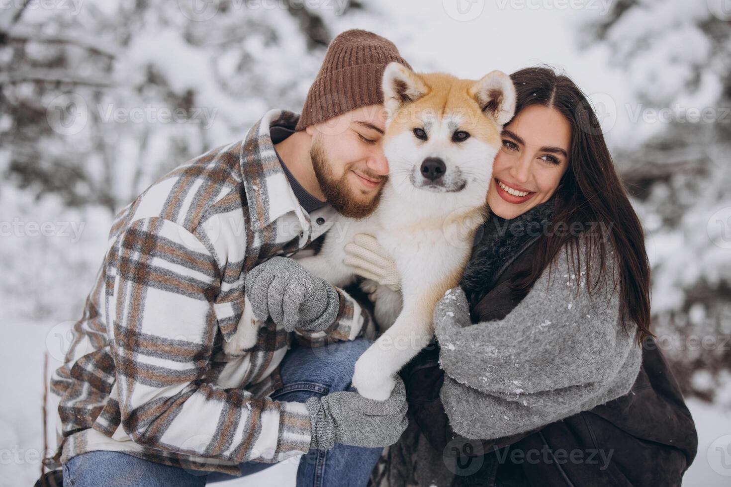 Happy young couple walking with akita dog in forest on winter and snowly day photo