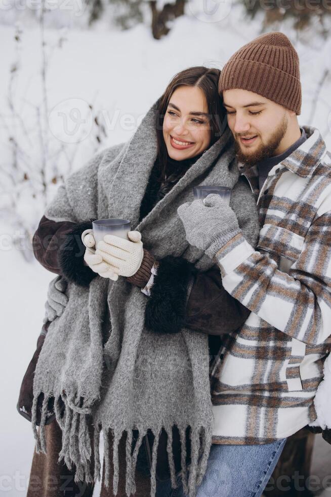 Happy beautiful couple resting and drinking hot tea in the forest in winter in the mountains photo