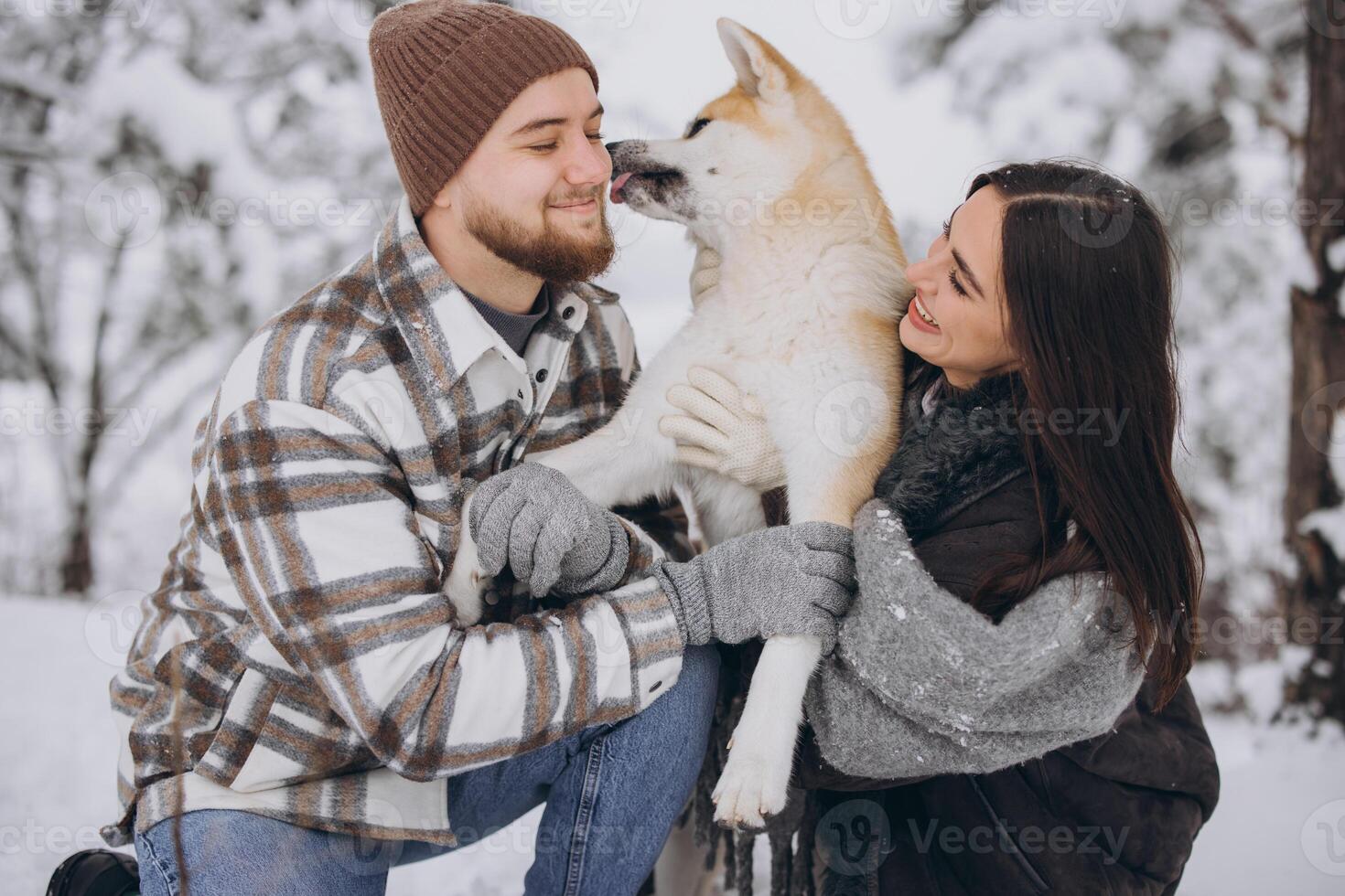 Happy young couple walking with akita dog in forest on winter and snowly day photo