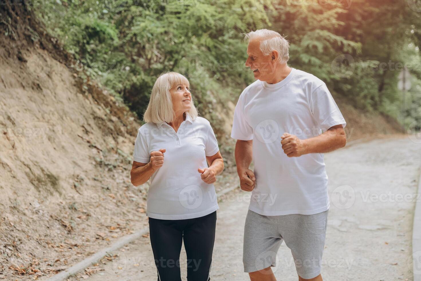 Running, sunshine and senior couple with fitness, exercise and bonding together with challenge. People in park, old man or mature woman with training, retirement and wellness with smile or lens flare photo
