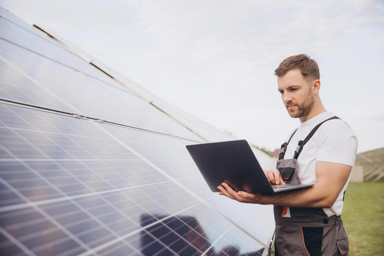 Engineer or construction worker bearded man uses laptop to check solar panel system status. Cell power plant. Augmented reality concept. Futuristic technology photo
