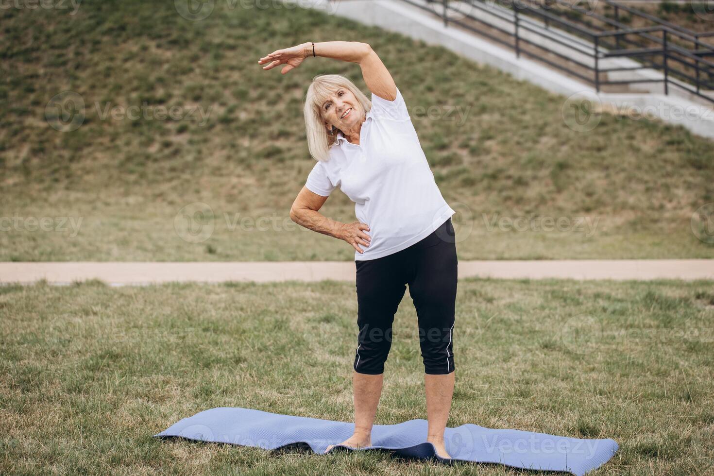 Senior Woman Exercising Outdoors on Yoga Mat, Performing Stretching Routine in Park photo