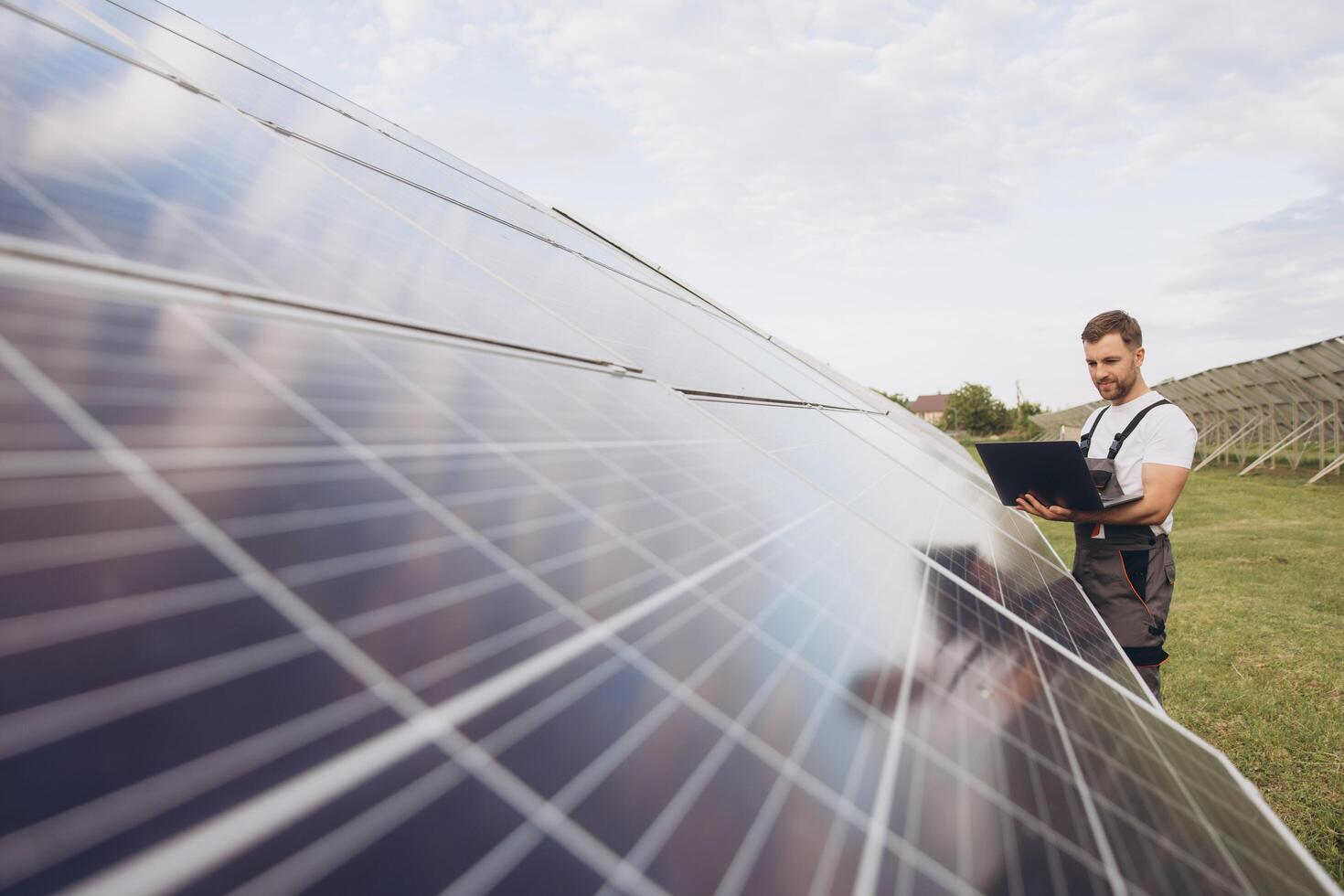 Engineer or construction worker bearded man uses laptop to check solar panel system status. Cell power plant. Augmented reality concept. Futuristic technology photo