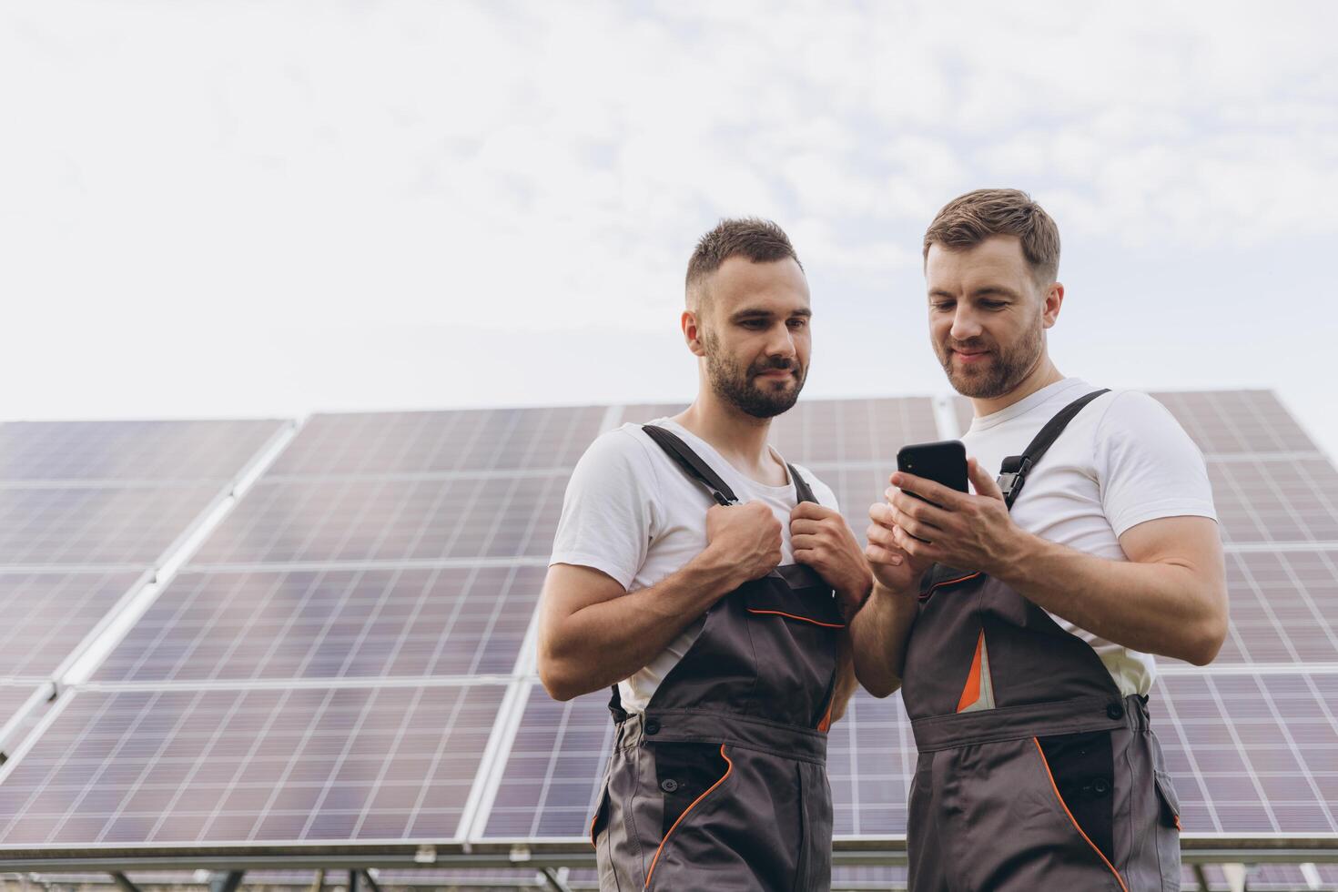 Energy specialist using digital smartphone reading information to check the efficiency of solar panel construction. Green energy jobs. Technology. Two solar power plant workers are recording data photo